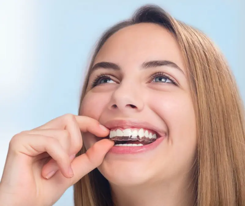 How to Clean Clear Aligners and Keep Them Clear Patient holding a clear aligner near her teeth